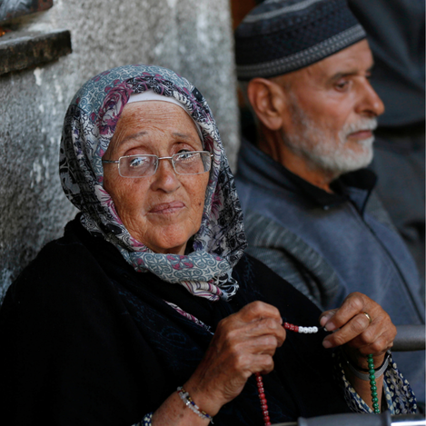 Elderly Palestinian refugees waiting in Gaza, holding prayer beads with resilience and dignity. Support UNRWA’s efforts to provide aid, healthcare, and hope for Palestine refugees in need.