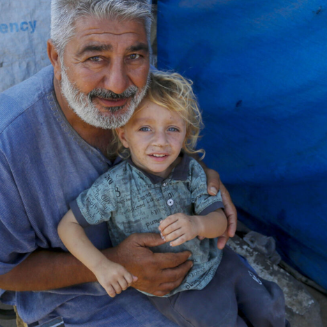 Adult holding child in Gaza shelter, highlighting need for humanitarian support